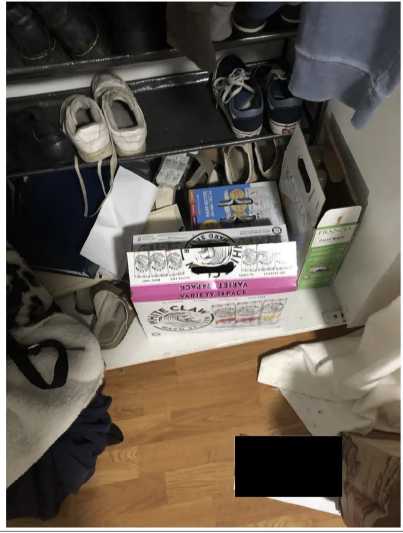 Shoe rack, shoes, beverage cartons and loose clothing on a closet floor, with a small black redaction.