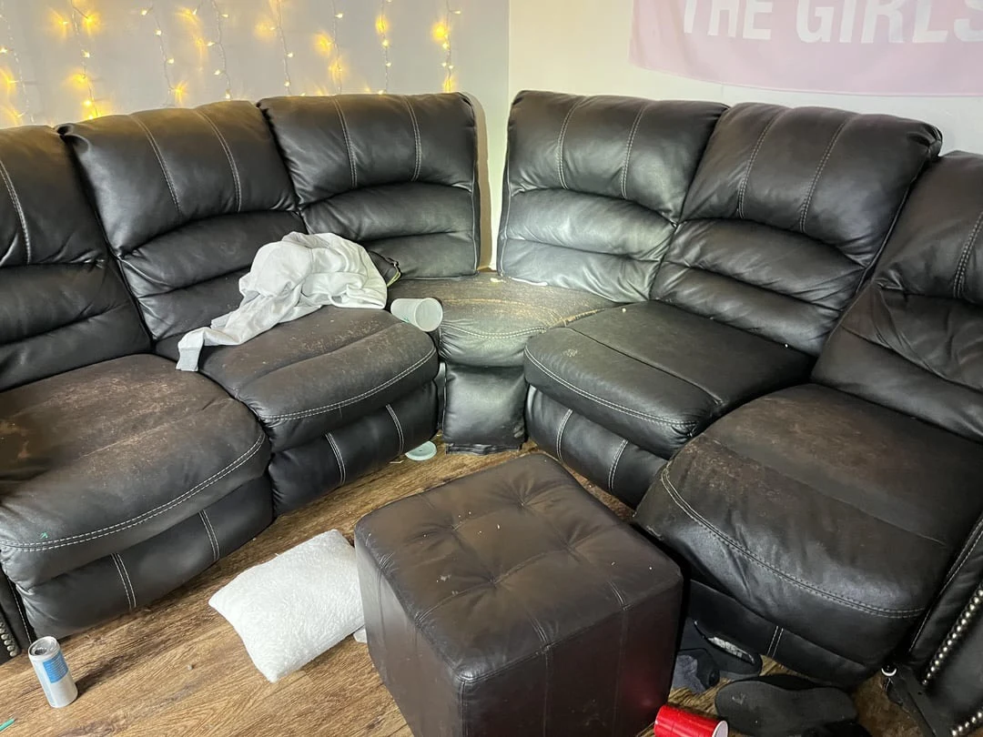 Black leather sectional seating and ottoman with a white blanket, pillows and scattered cups and cans.