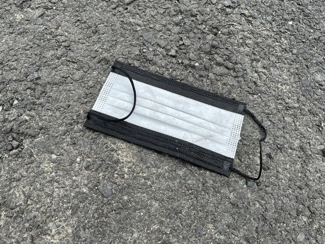 Close view of a black-and-white disposable face mask on rough asphalt.