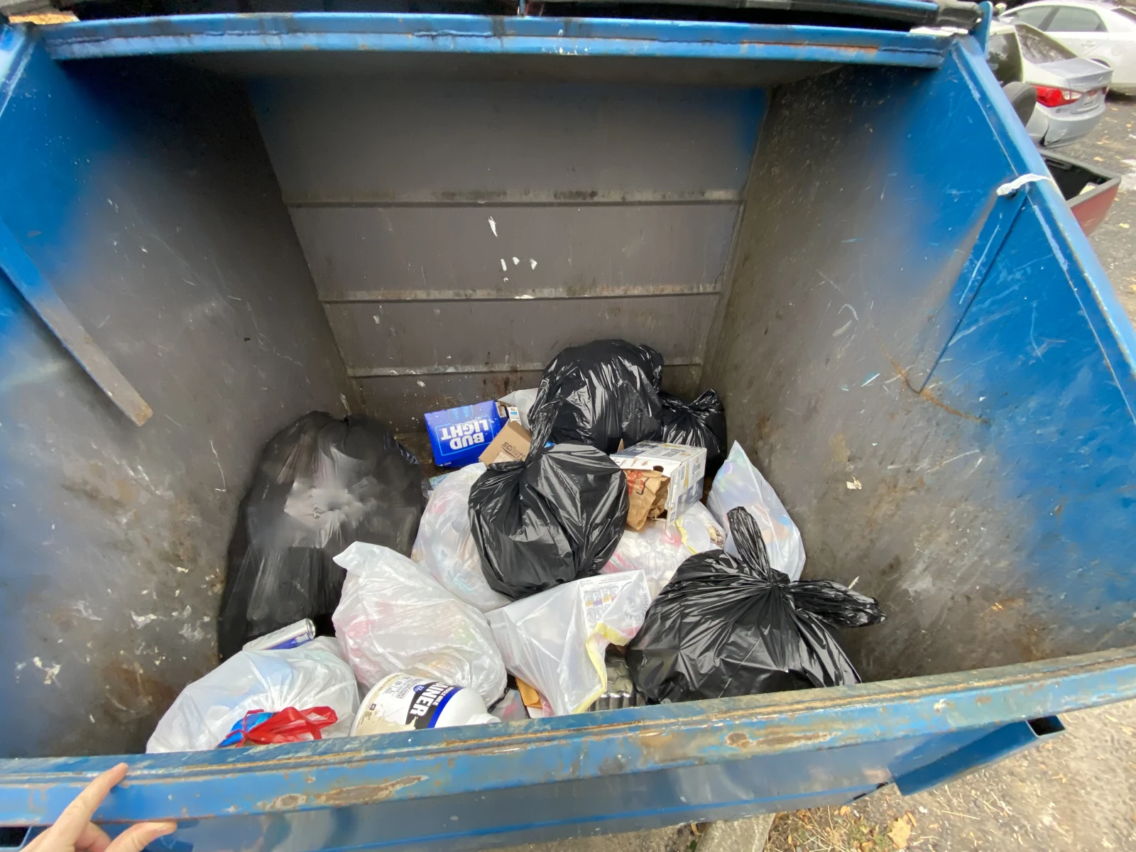 View into a blue dumpster containing black and white trash bags, cartons and loose packaging.