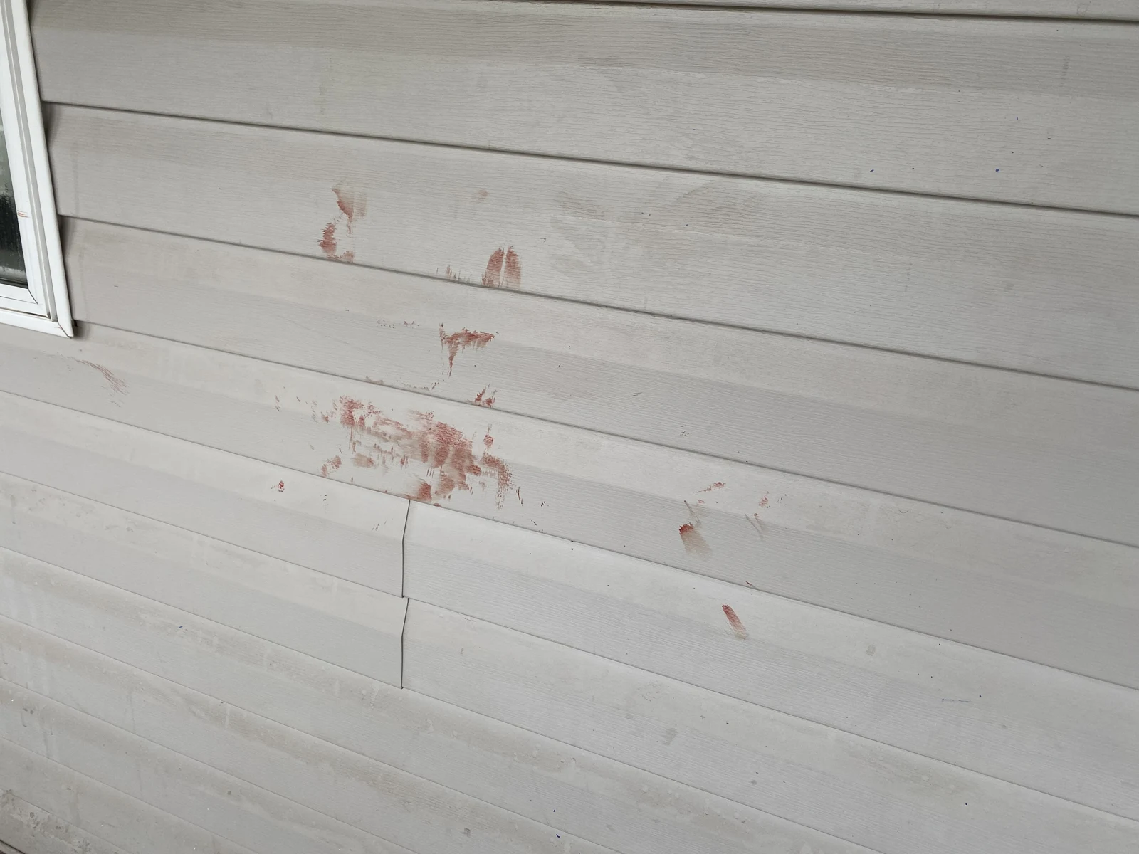 Reddish smears and streaks on pale horizontal exterior siding.