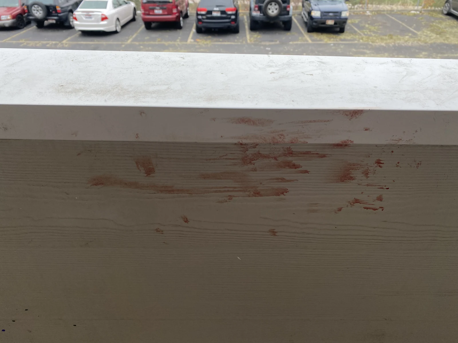 Close view of reddish horizontal smears on a pale balcony railing, with cars in the background.