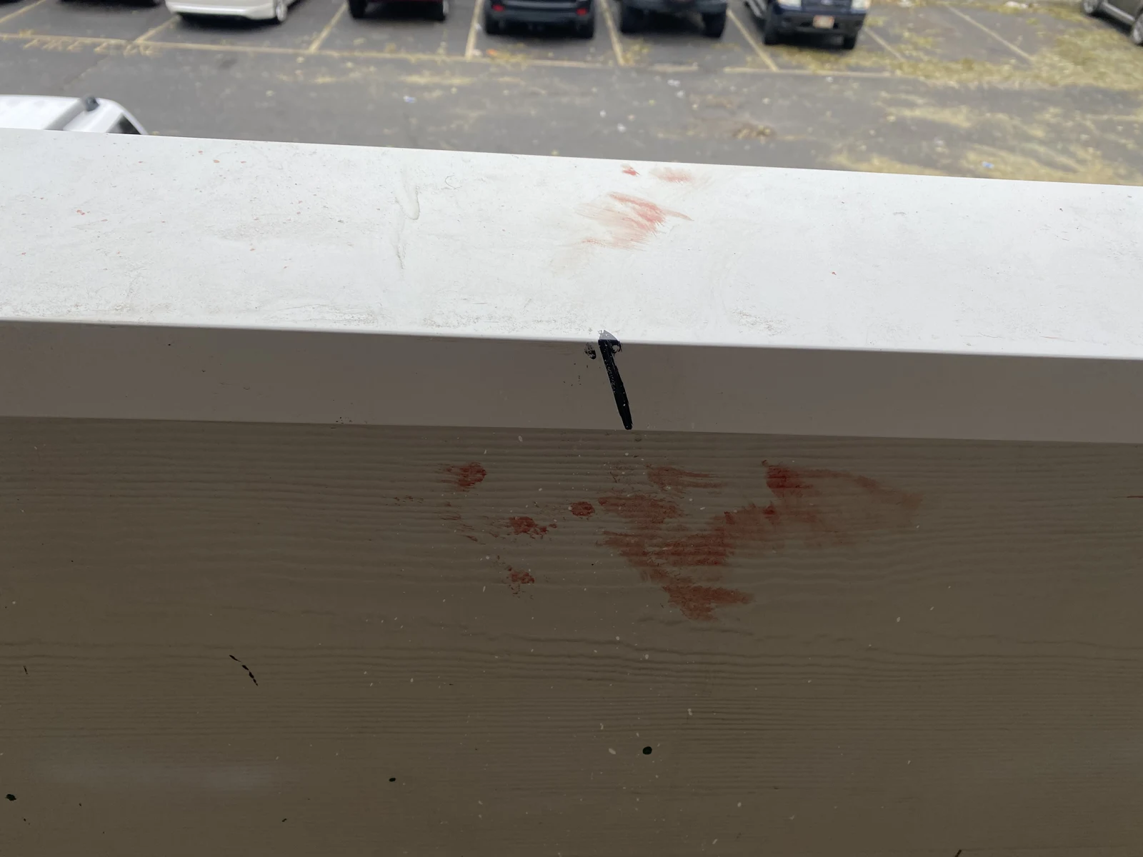 Reddish marks on the face and top of a balcony railing, with a small black marker and cars beyond.