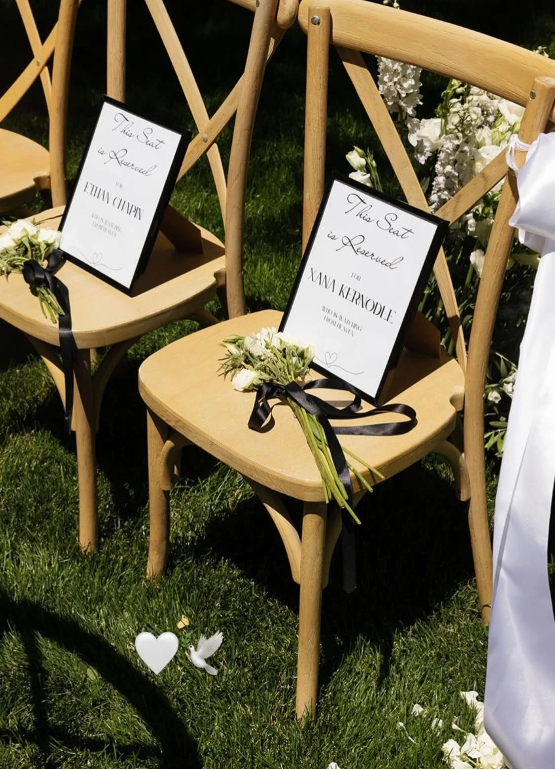 Two wooden chairs on grass with memorial place cards and small flower arrangements tied with black ribbons.