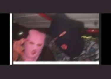 Low-resolution photograph of two people wearing pink and dark ski masks in an indoor setting.