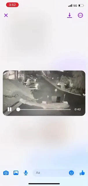 Phone video-viewer screenshot of an overhead nighttime parking area with cars, bins and a curved roadway; playback shows 0:42 remaining.