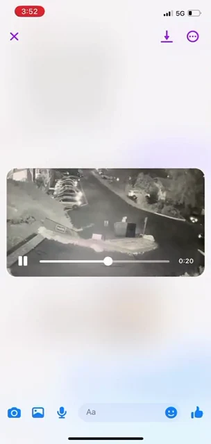 Phone video-viewer screenshot of an overhead nighttime parking area with cars, bins and a curved roadway; playback shows 0:20 remaining.