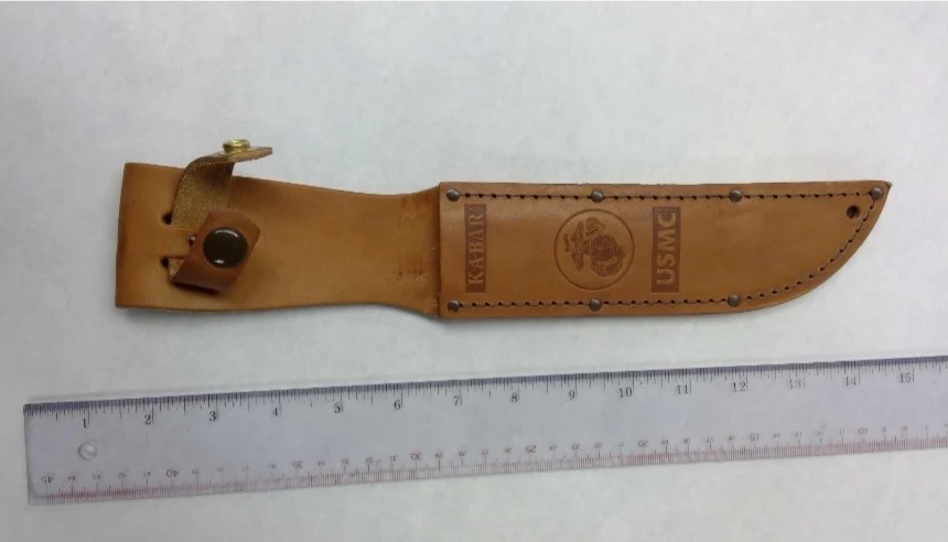 Front of a brown leather knife sheath marked KA-BAR and USMC, photographed horizontally above a clear ruler.