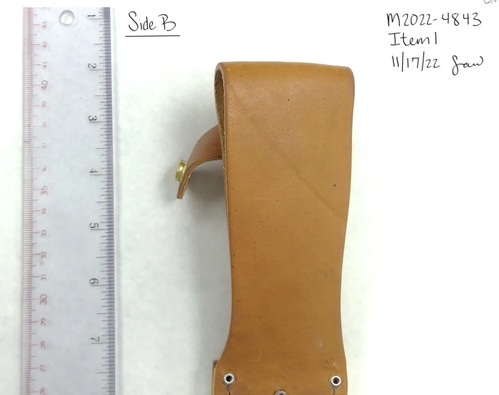 Close photograph of the back of a leather sheath strap beside a clear ruler, labeled Side B.