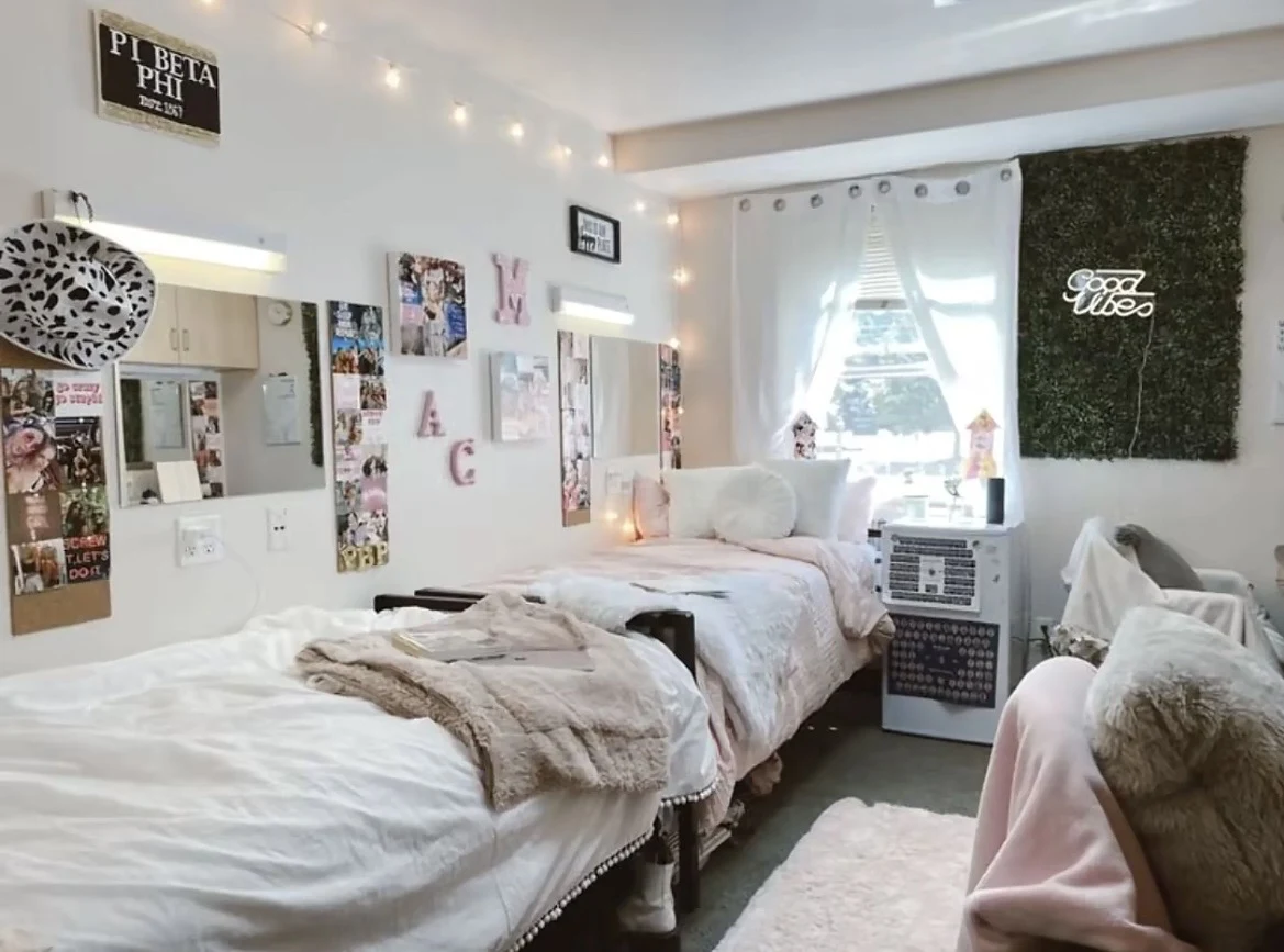 Bright bedroom with two beds, a curtained window, string lights, wall photographs, a green wall panel and a Pi Beta Phi sign.