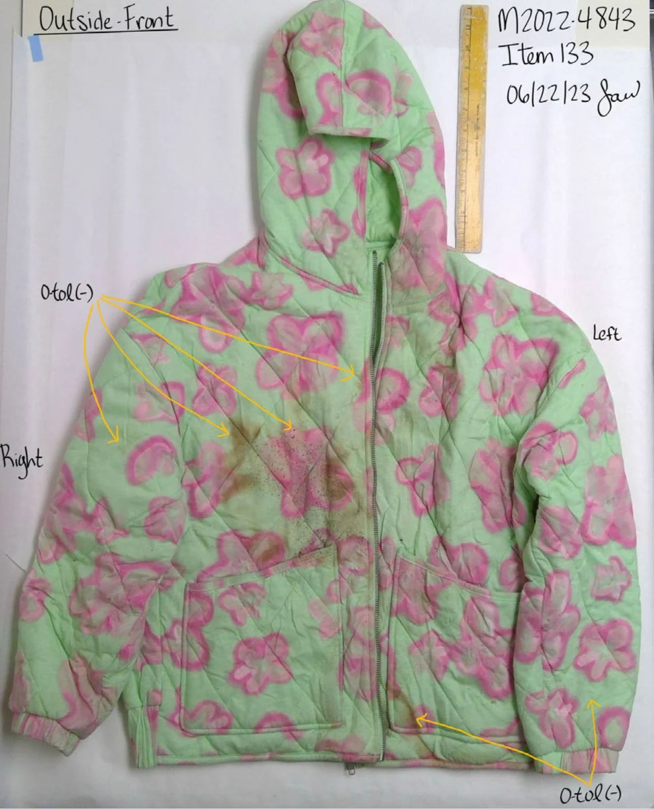 Front of a green quilted hooded jacket with pink flower patterns, beside a yellow ruler and handwritten testing annotations.