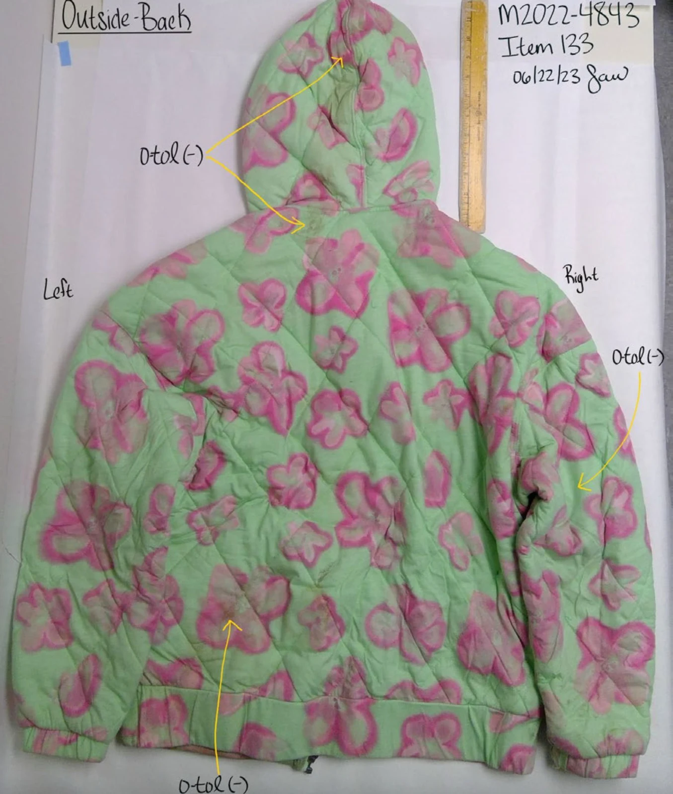 Back of a green quilted jacket with pink flower patterns and hood, with arrows marking annotated testing areas.