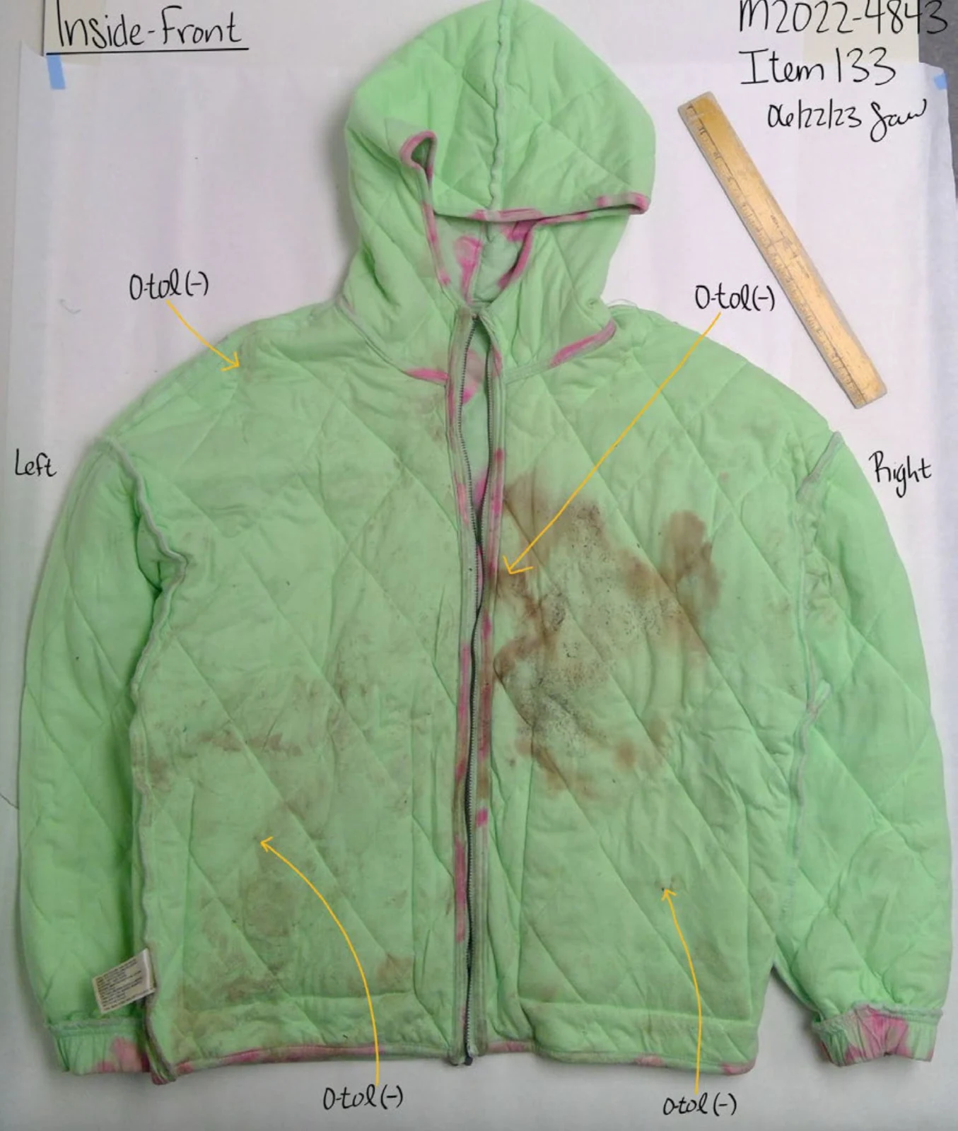 Inside front of a green quilted hooded jacket, showing brown discoloration and annotated arrows beside a ruler.