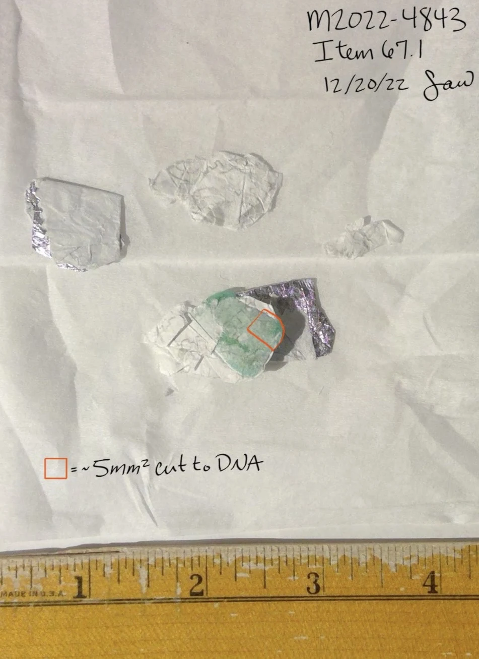 Small foil and pale wrapper pieces on white paper beside a yellow ruler, with an orange outline identifying a cut sample area.