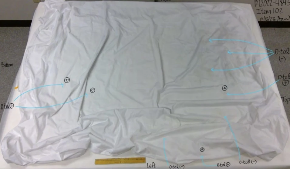Large white fabric sheet laid out with wrinkles, a yellow ruler, circled labels and blue testing arrows.