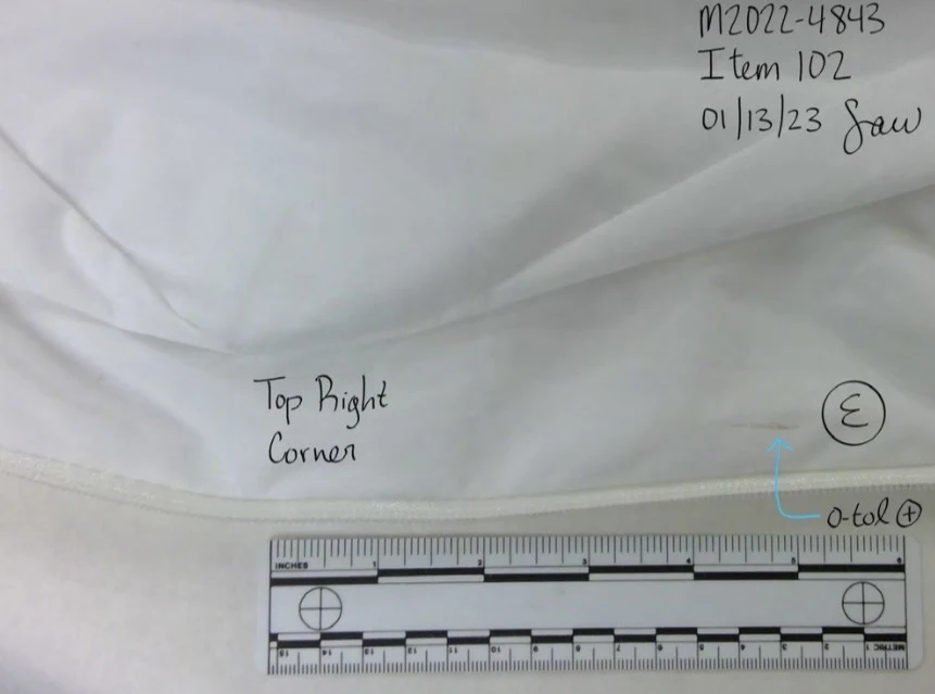 Close photograph of a white fabric seam labeled top right corner, beside a measurement scale and blue arrow.