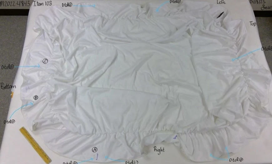 White gathered fabric sheet laid out beside a yellow ruler, with handwritten edge labels and blue arrows.