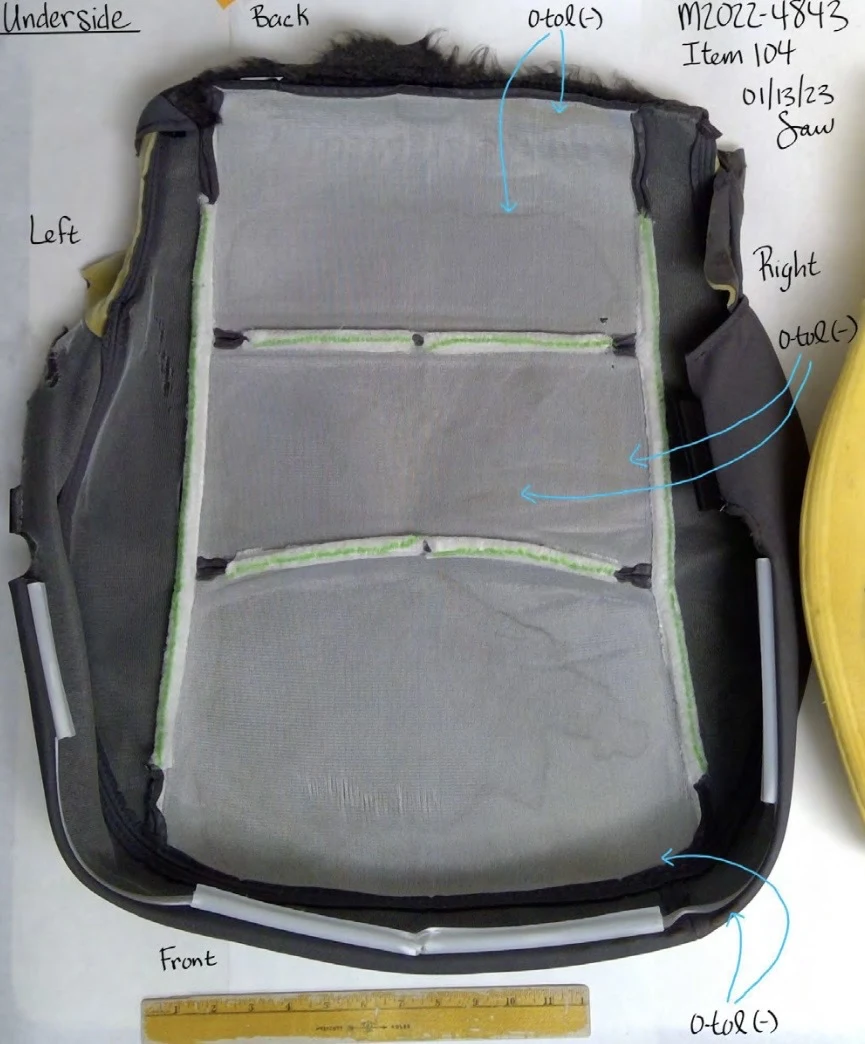 Underside of a removed vehicle seat cover showing gray backing, seams, black edging and annotated arrows.