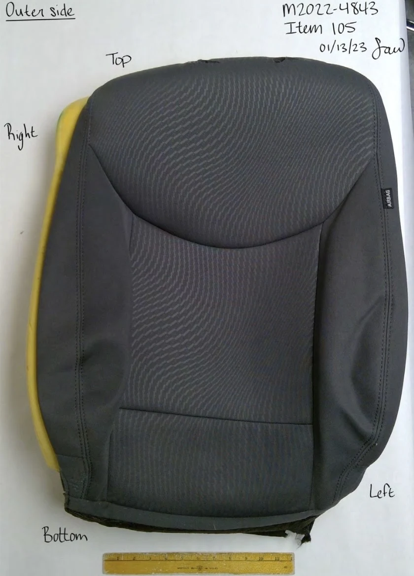 Dark patterned vehicle seat-back upholstery with yellow foam visible around the edges, labeled outer side.