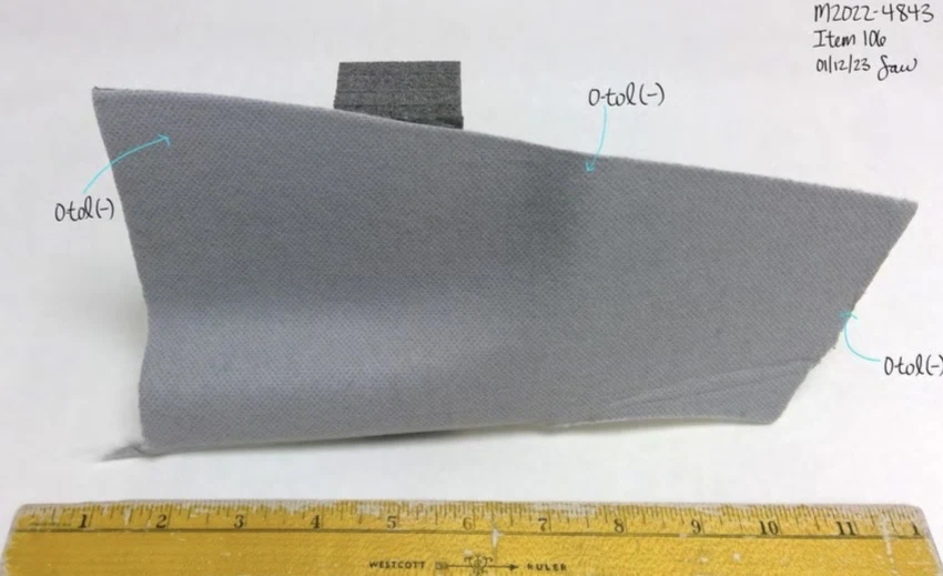 Gray angled fabric panel with a black fastening tab, photographed beside a yellow ruler and annotated arrows.