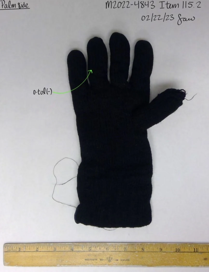 Palm side of a single black knitted glove with loose threads beside a yellow ruler.