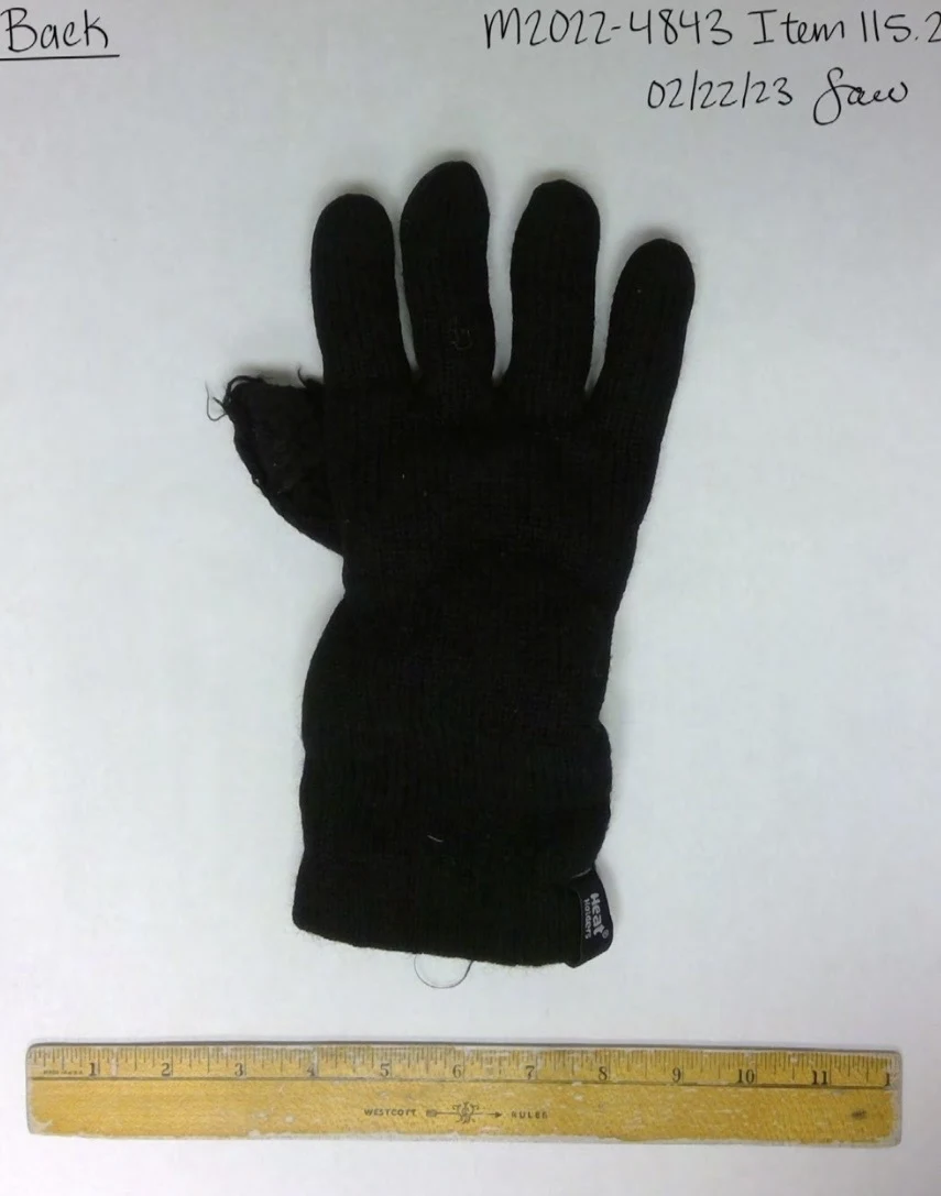 Back of a single black knitted glove with loose threads near a finger, beside a yellow ruler.