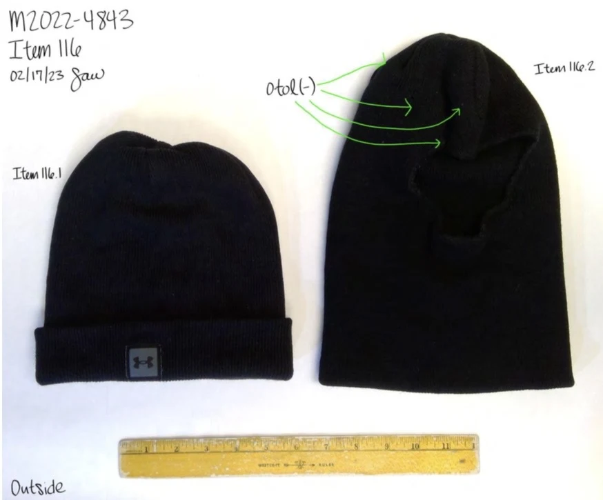 Two black knit caps beside a yellow ruler; one has an Under Armour logo and the other has green testing arrows.
