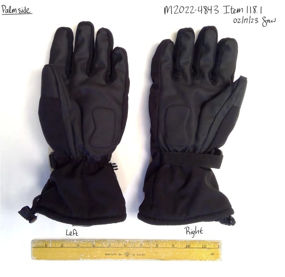 Palm sides of black winter gloves with reinforced padded sections, wrist straps and long cuffs, beside a ruler.
