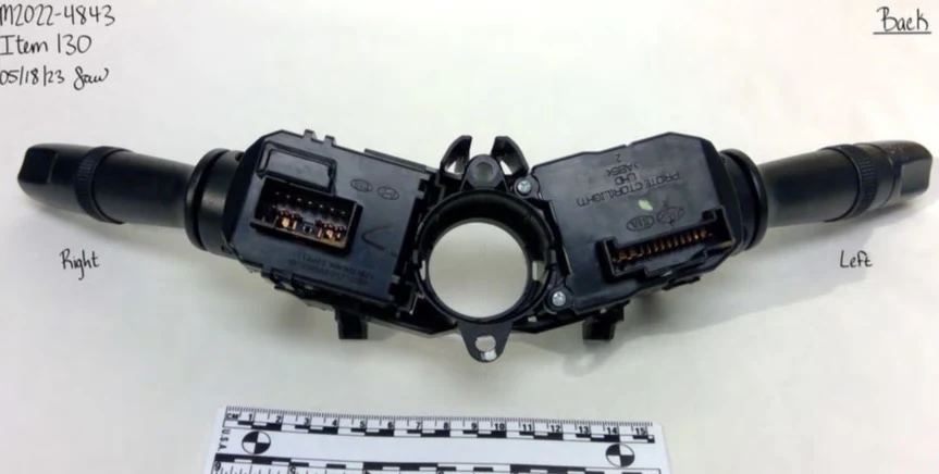 Back of a vehicle steering-column switch assembly showing electrical connector sockets and two control stalks, beside a measurement scale.
