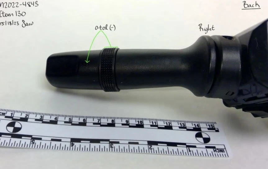 Close view of one black control stalk from the back of a steering-column switch assembly, with a textured rotating band and measurement scale.