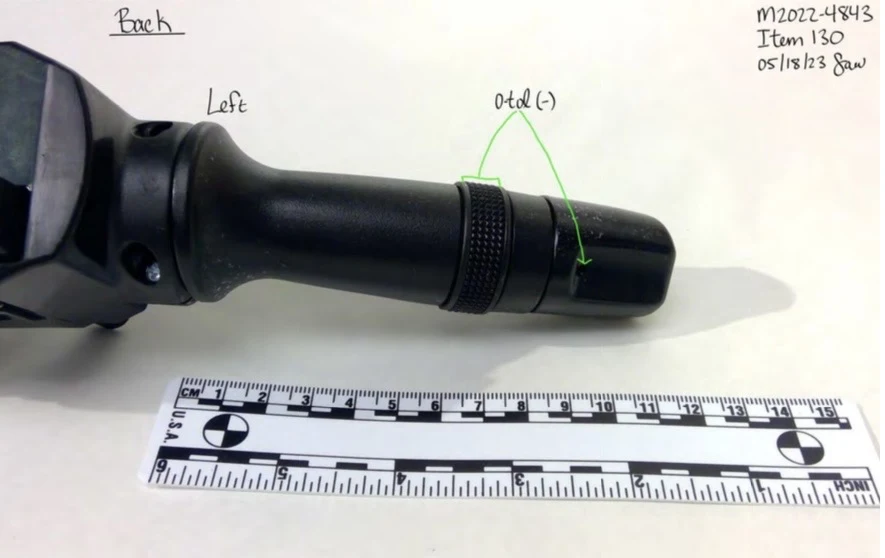 Close view of the opposite black control stalk from a steering-column switch assembly, with a rotating band, arrows and measurement scale.