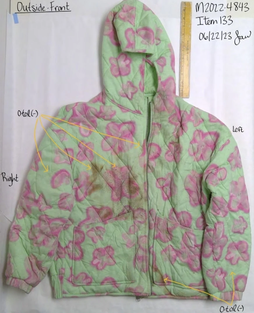 Front of a green quilted hooded jacket with pink flower patterns, a yellow ruler and handwritten test-area arrows.