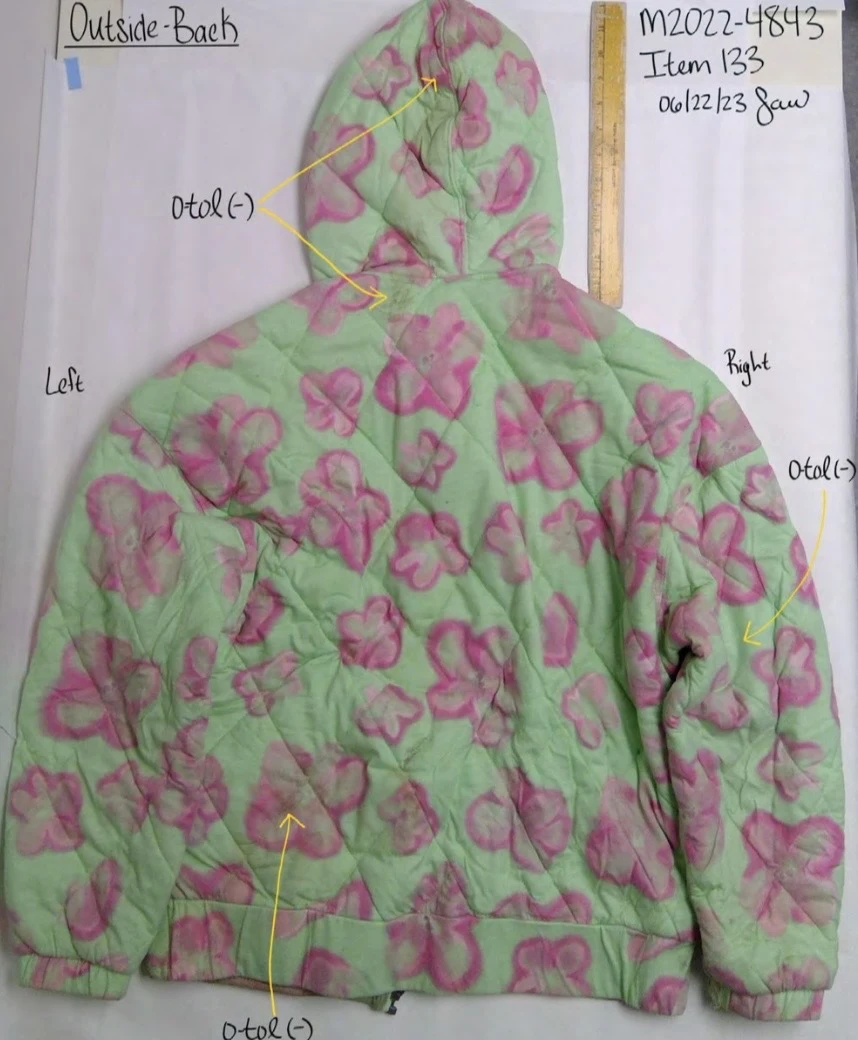 Back of a green hooded jacket with pink flowers, yellow arrows and a ruler along the side.