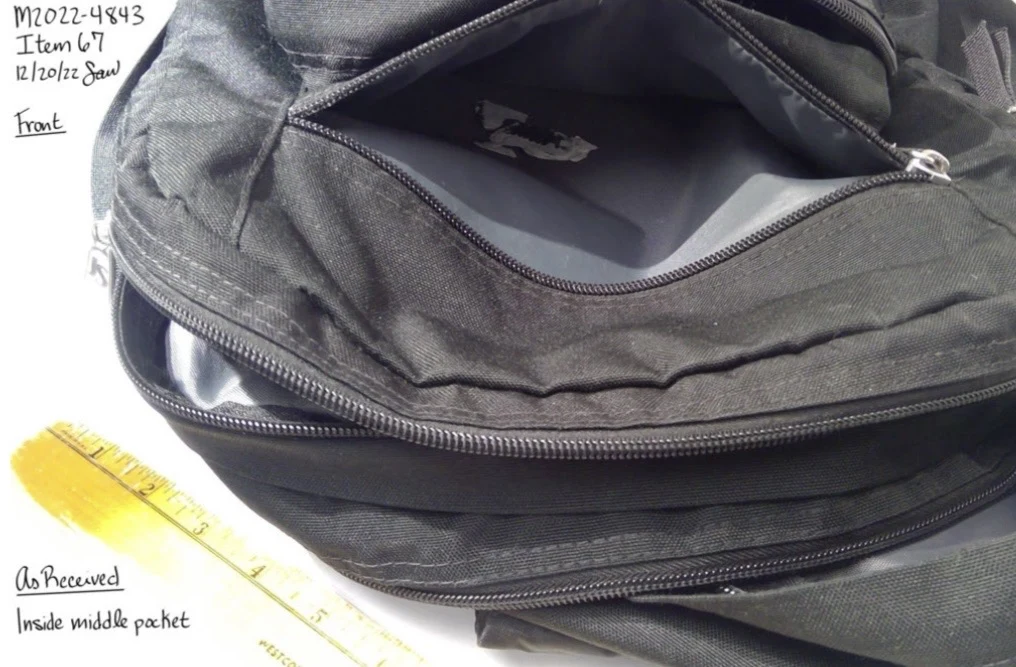 Close photograph inside an open black backpack pocket with a small pale object visible and a yellow ruler nearby.