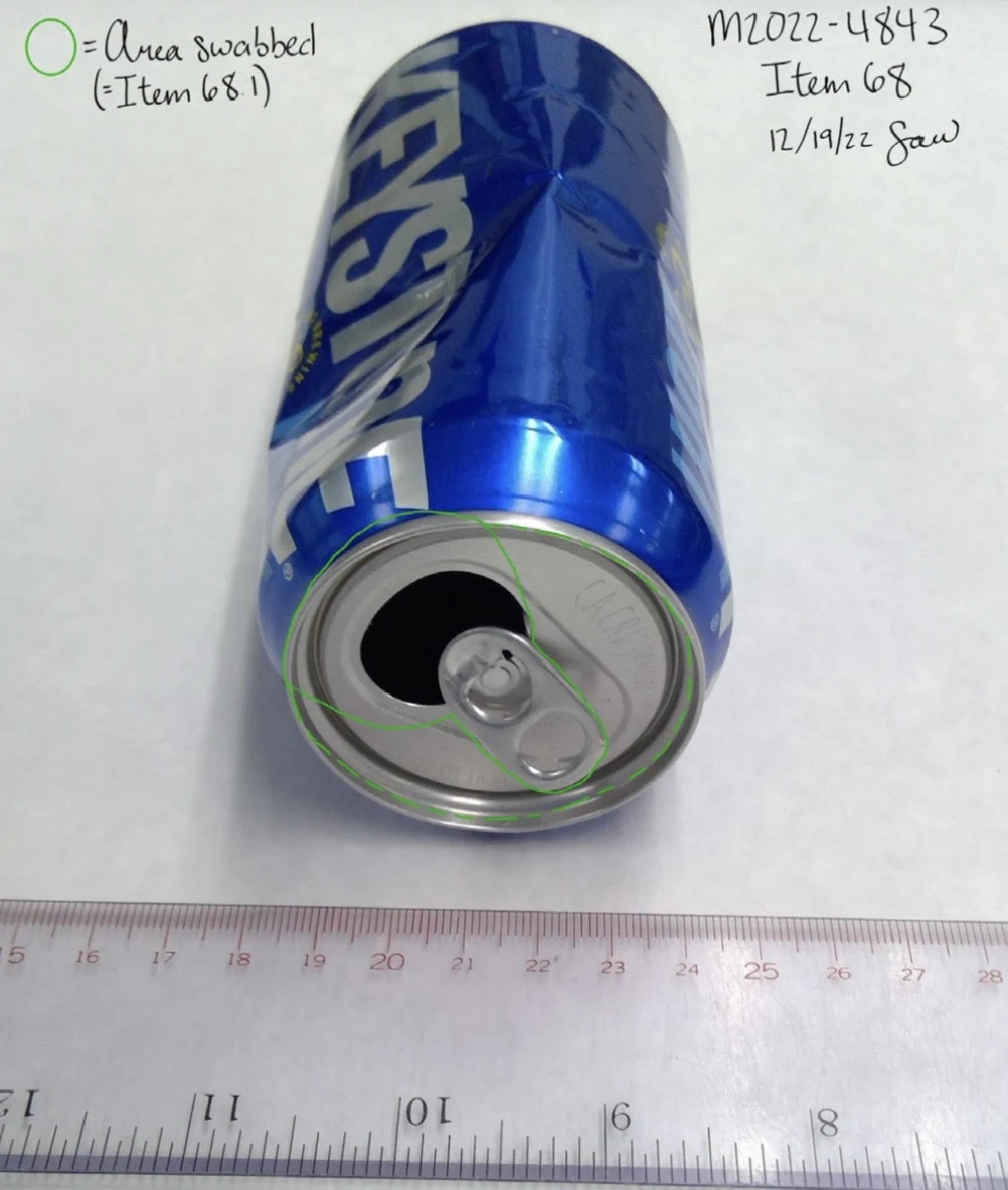 Blue Keystone can with an open pull tab and dented side, photographed beside a ruler with a green outline around the top rim.