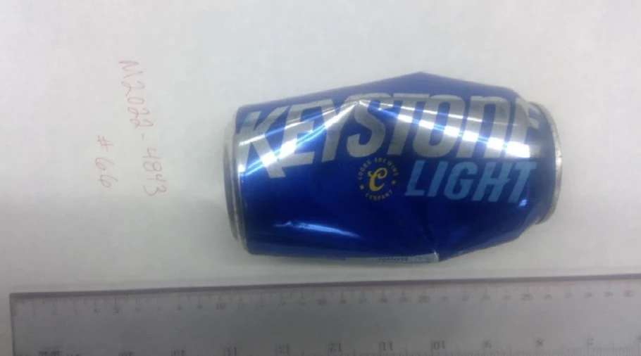 Side of a dented blue Keystone Light can resting horizontally above a ruler, labeled item 66.