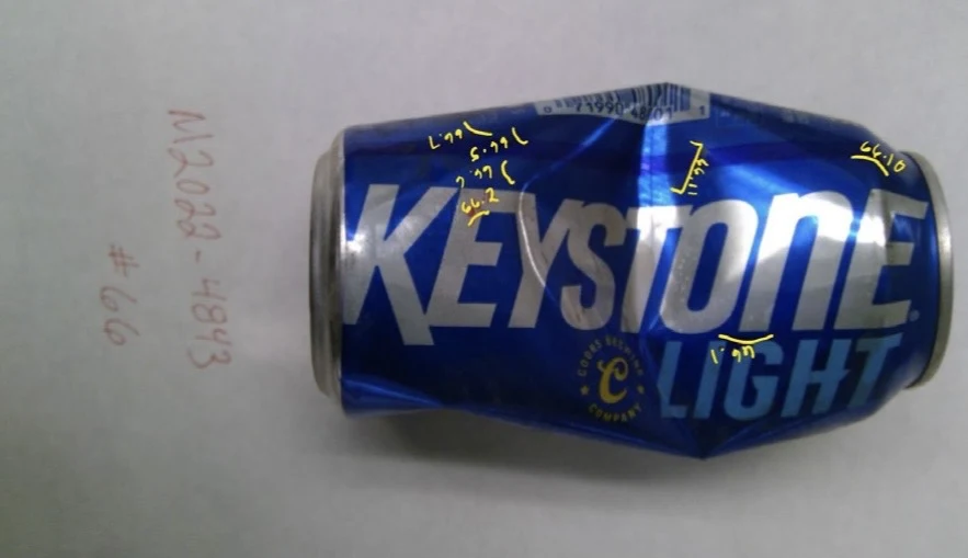 Dented blue Keystone Light can with yellow handwritten sample marks across its side, labeled item 66.