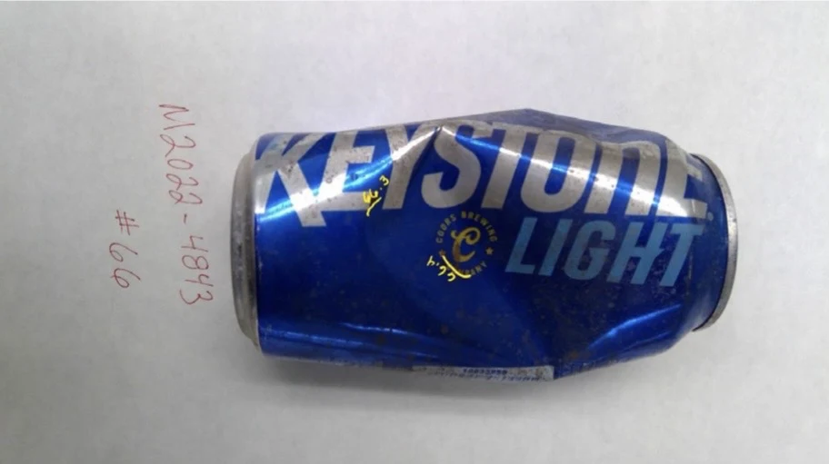 Alternate side view of a dented Keystone Light can with yellow handwritten marks, labeled item 66.