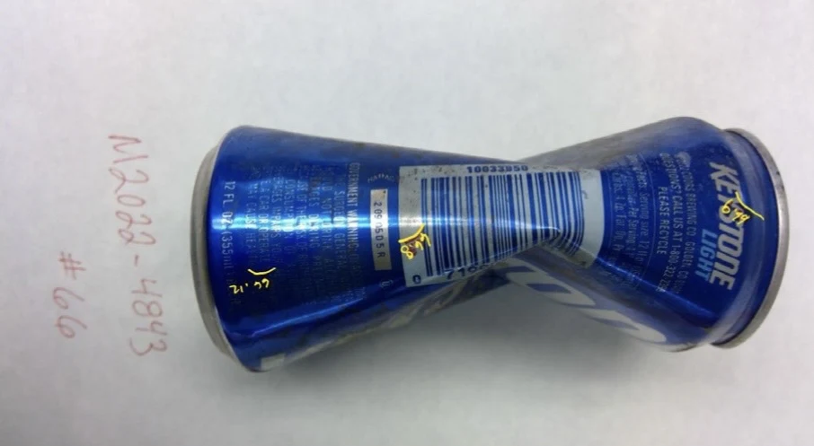Barcode side of a crushed blue Keystone can with yellow handwritten sample marks, labeled item 66.