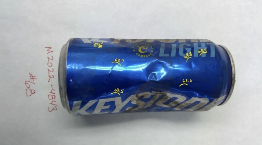 Side view of a blue Keystone Light can with a central dent and yellow handwritten sample marks, labeled item 68.