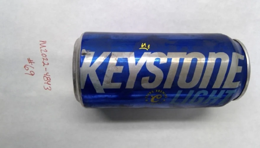 Blue Keystone Light can photographed horizontally, with yellow handwriting above the logo and item 69 on the background.