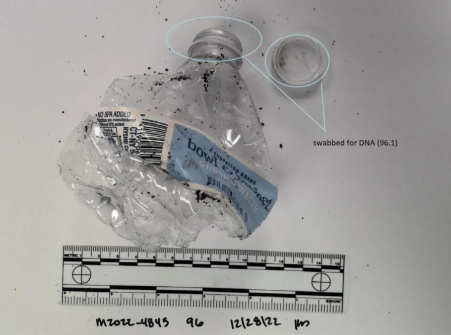 Crushed clear plastic water bottle with blue label, detached cap and dark particles, above a scale with the mouth and cap circled.