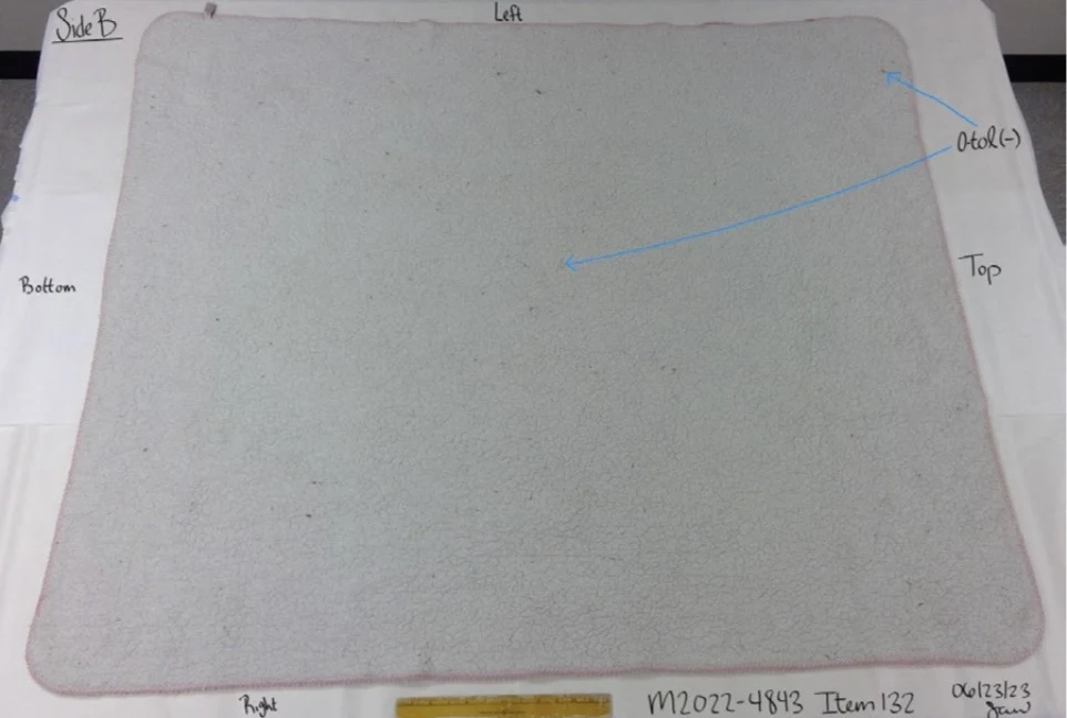 Plain gray back of a pink-edged rectangular mat, beside a ruler with blue testing arrows.