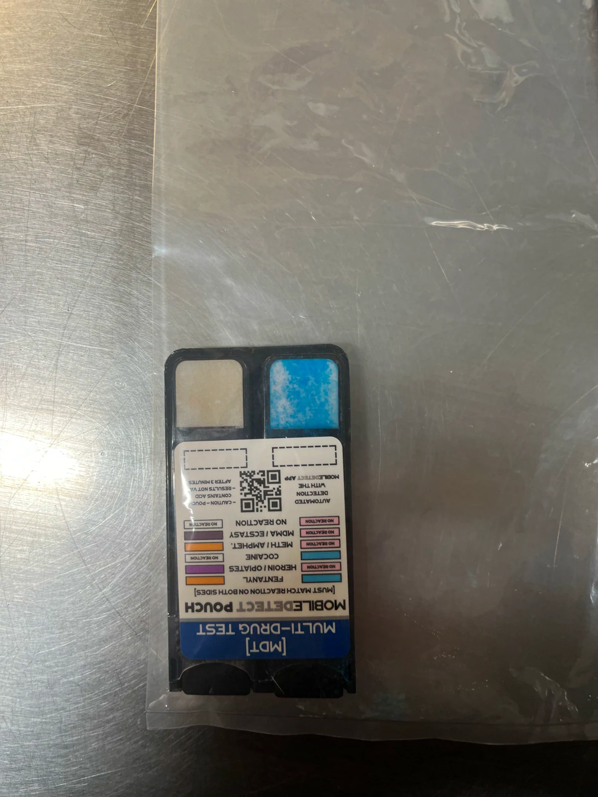 MobileDetect multi-drug test pouch with two rectangular panels, one blue, resting on a clear plastic bag on a metal surface.