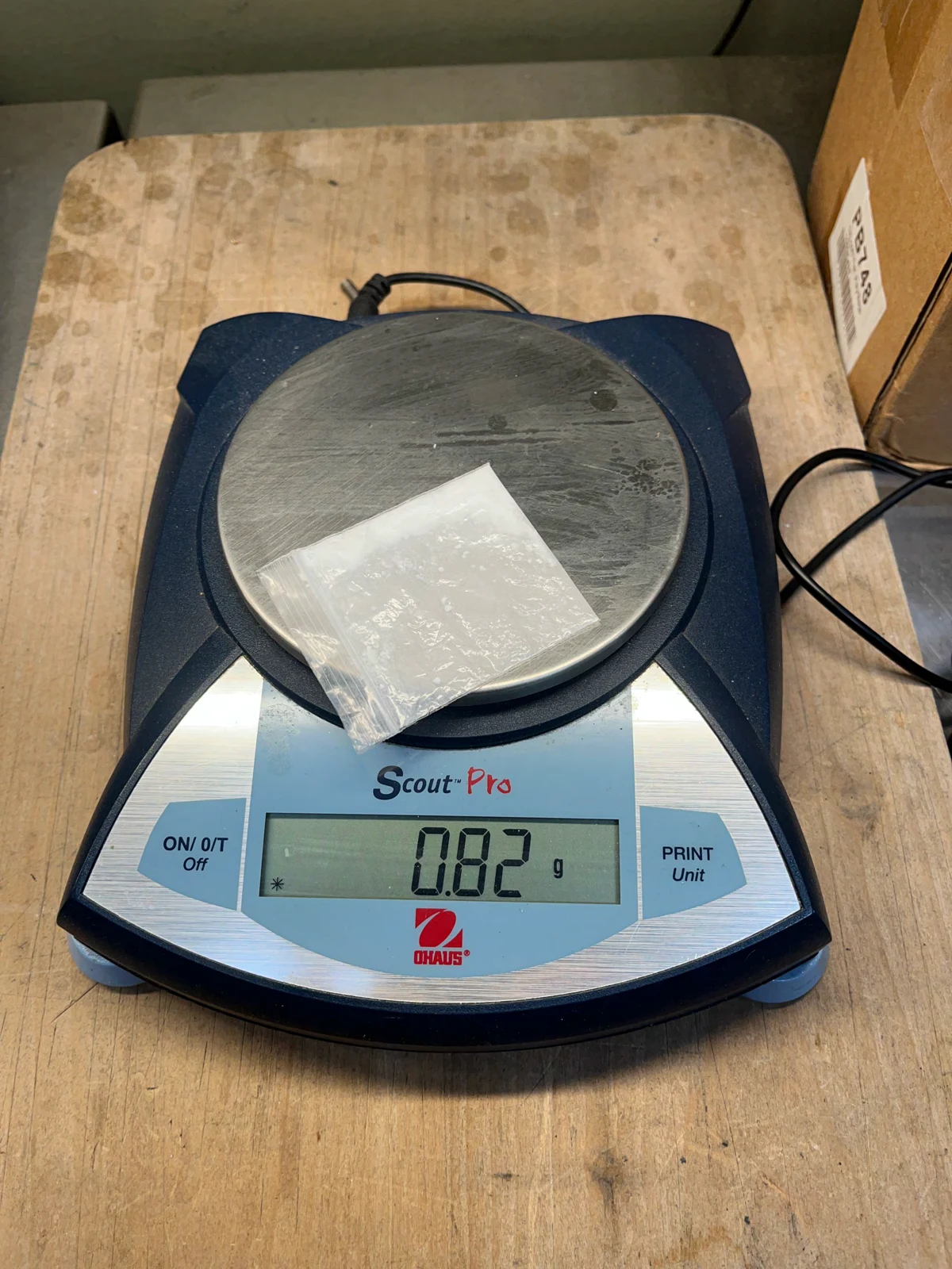 Alternate photograph of a clear bag on a Scout Pro digital scale displaying 0.82 g, with a cord and cardboard box beside it.