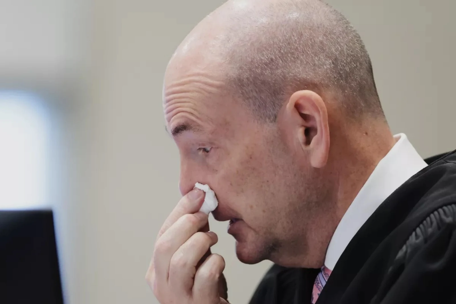 Close view of a person in a dark judicial robe holding a tissue against the nose.