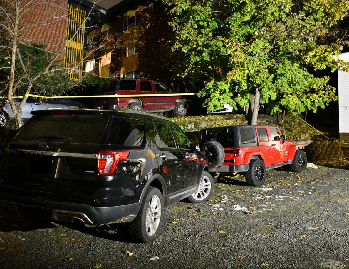 Black SUV and red Jeep parked beside a retaining wall and trees.