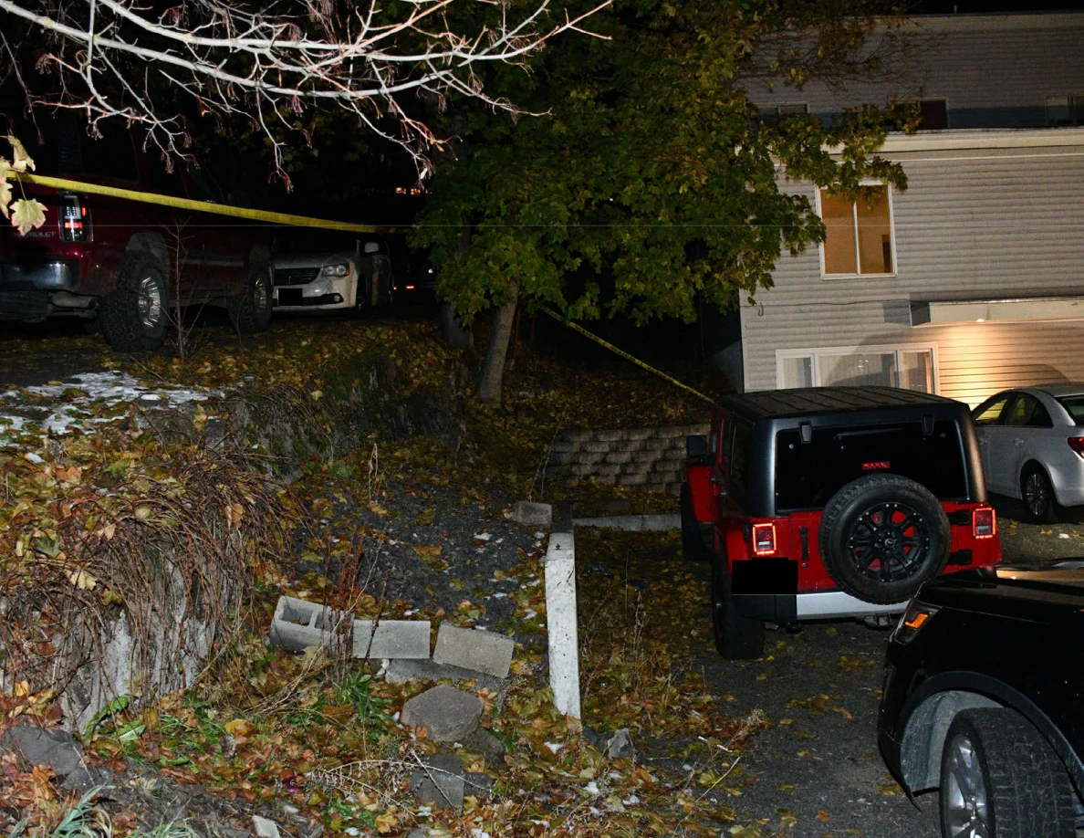 Red Jeep, parked vehicles, retaining wall, trees and yellow barrier tape.