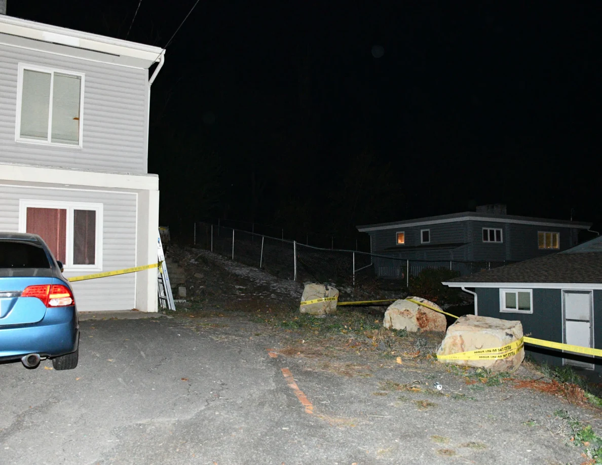 Side of a house, blue car, boulders, fence and yellow barrier tape.