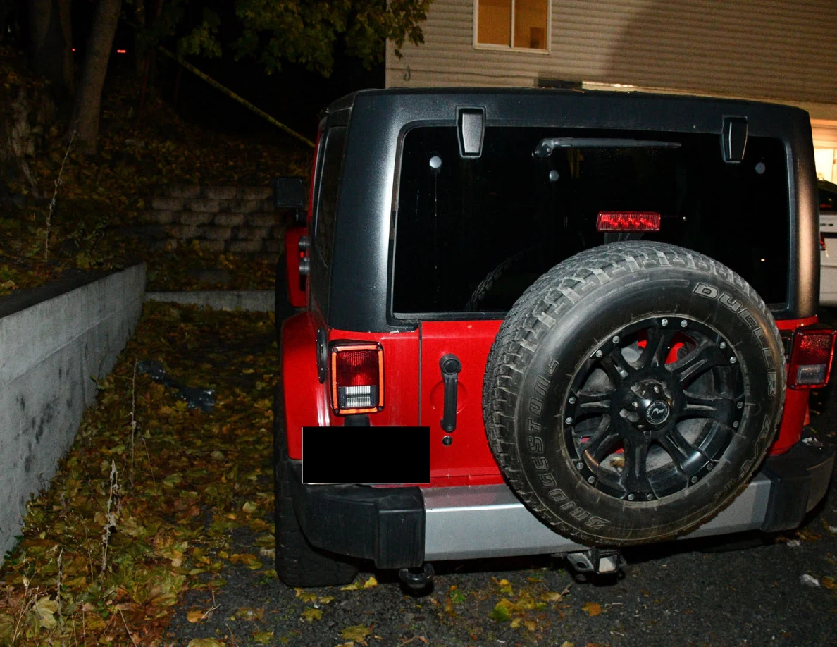 Rear of a red Jeep with a spare tire and redacted license plate.